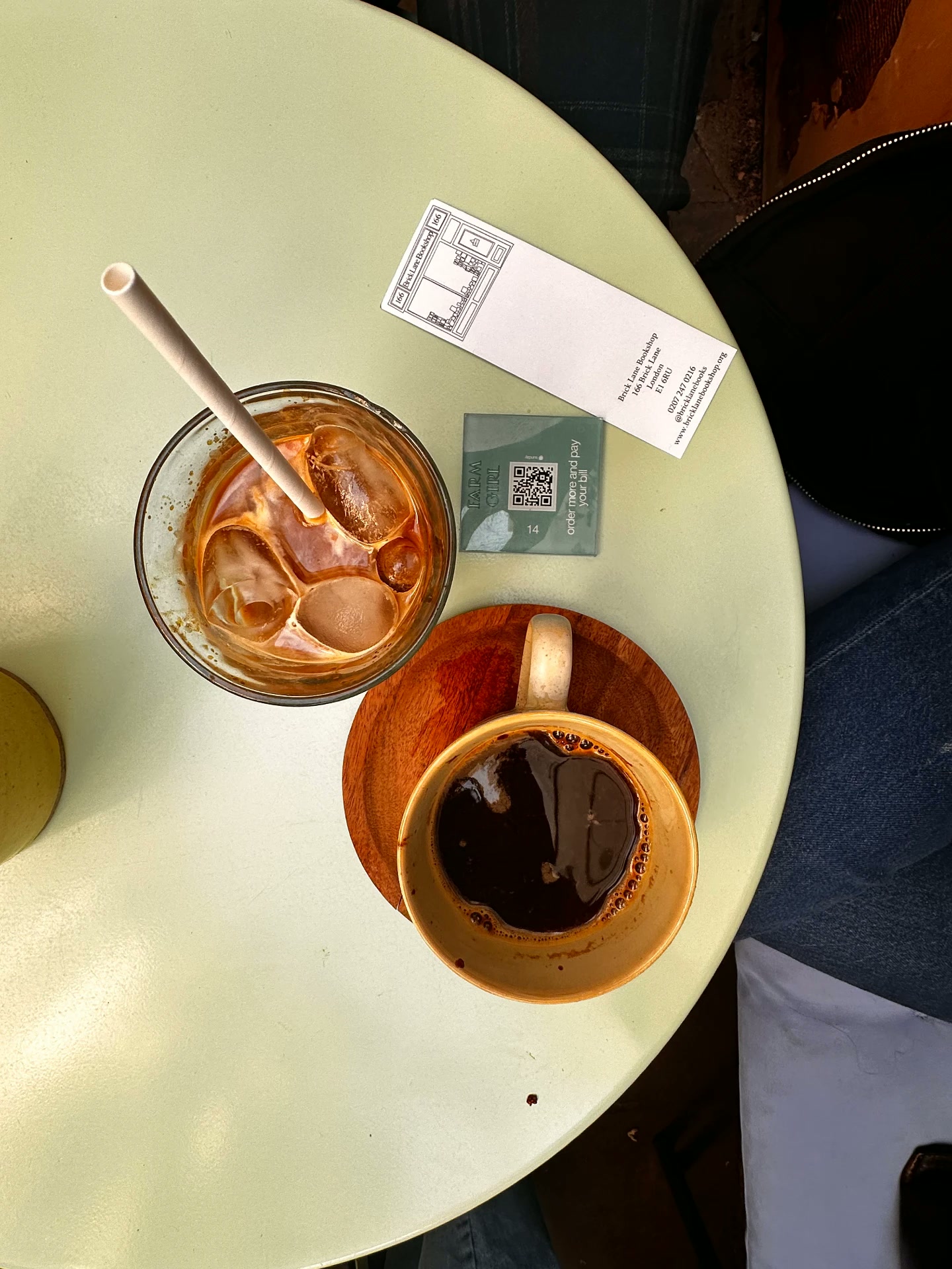 Two coffees on a pale green table: an iced milk coffee and a black filter coffee